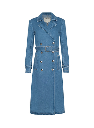 The Bradley Trench Coat is a long, blue medium-wash denim trench with a notched collar, double-breasted front, silver buttons, waist belt, and buttoned cuff straps. Crafted from lightweight denim and shown against a white background.