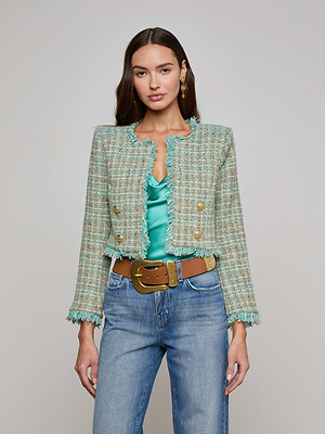 A woman wears the L'AGENCE Sale Clydie Cropped Tweed Jacket—green, collarless, with gold-tone buttons and fringe—over a satin teal top, blue jeans, and a wide brown belt as she faces the camera against a plain background.