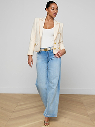 A woman wearing the Wylla Tweed Blazer—featuring a neutral ecru hue and embroidered trim—paired with a white top, light blue wide-leg jeans, and sandals walks confidently against a plain white background.