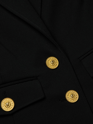 Close-up of the Wylla Blazer in black stretch suiting, showcasing three gold lion head buttons with text, two flap pockets, and visible stitching details.