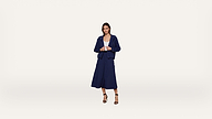 A woman stands against a plain white background wearing a navy blue jacket and culottes, a white top, and black heeled sandals.