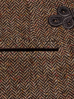 Close-up of the Gable Herringbone Blazer by L'AGENCE—crafted from Italian recycled wool in brown and beige herringbone, featuring a horizontal pocket and a black braided decorative knot at the upper right corner.