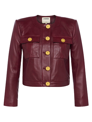 The Deidra Cropped Leather Jacket is a burgundy Italian lambskin piece featuring a collarless, round neckline, long sleeves, front flap pockets, and bold gold buttons down the center and on the pockets. It offers a fitted silhouette.
