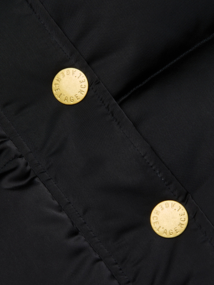 Close-up of the Kataleya Puffer Coat, a black water-repellent jacket with two gold metallic buttons engraved with text, sewn along a diagonal seam.