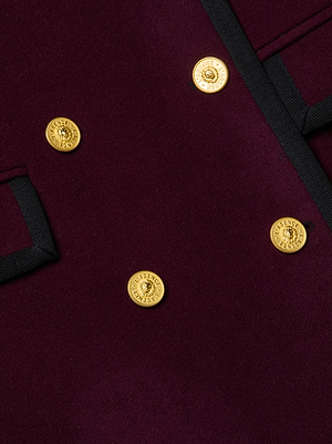 Close-up of the Irene Long Coat by L'AGENCE, made from Italian recycled wool in maroon with black trim and four shiny gold buttons on the front and pocket flap.