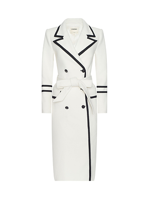 The Irene Long Coat is a white, knee-length belted trench with black-trimmed collar, lapels, cuffs, and edges. Its double-breasted front and long sleeves make it the perfect statement for New York Fashion Week Fall 2026.