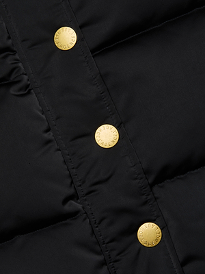 Close-up of the Nalo Faux Fur Puffer Vest by L'AGENCE, featuring black quilted fabric, shiny gold snap buttons embossed with text, and smooth, slightly padded construction—perfect for cold weather.