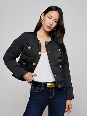 A woman with long dark hair poses confidently against a plain background wearing the Juana Scarf Puffer Jacket, styled with a white top, dark jeans, a black belt with a gold buckle, and gold hoop earrings.