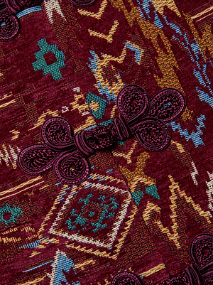 Close-up of the Asha Jacquard Jacket by L'AGENCE, showcasing its maroon tapestry print with teal, yellow, and white geometric patterns and matching maroon braided frog closures. The jacket's rich texture and detailed design are clearly visible.