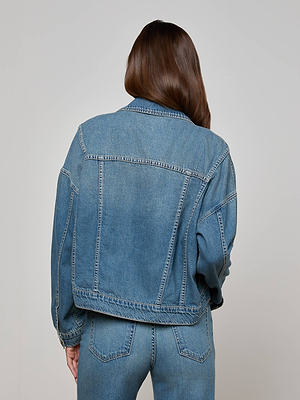 A person with long brown hair is seen from behind, wearing the L’AGENCE Vianney Jean Jacket and matching blue denim jeans against a plain light background.