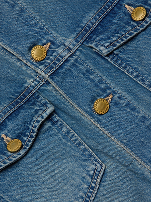 Close-up of the Vianney Jean Jacket by L'AGENCE, featuring intersecting seams and four gold metal buttons embossed with text. Detailed stitching and textured denim emphasize its relaxed fit and timeless craftsmanship.