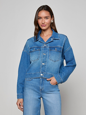 A woman with long brown hair and subtle makeup stands against a plain background, wearing the Vianney Jean Jacket in a light wash with matching jeans, looking at the camera with a slight smile.