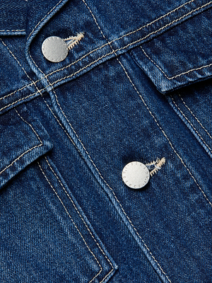 Close-up of the Vianney Jean Jacket in indigo wash blue denim, showing white stitching, two metal buttons, and part of a flap pocket.
