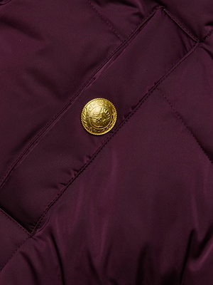 A close-up of maroon quilted satin with diagonal stitching from the L'AGENCE Violeta Reversible Puffer, featuring a single gold decorative button with an ornate crest design.