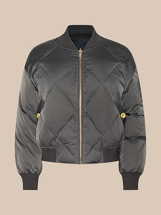 Violeta Reversible Puffer—black quilted satin bomber jacket with gold zipper and buttons, featuring ribbed cuffs, hem, and collar—is displayed on a light beige background.