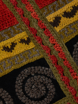 Close-up of colorful yarn embroidery on black fabric, with red, yellow, olive green, and brown threads in geometric and spiral patterns—perfect for adding flair to the Kada Crochet Coat or any patchwork outerwear.