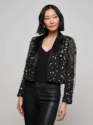A woman with a short bob wears the Soma Embellished Blazer—black with hand-applied crystals and shining accents—over a black top and leather pants, standing against a plain light gray background.