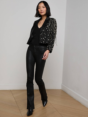 A woman stands in a corner against a neutral background and wooden floor wearing the Soma Embellished Blazer, styled with a black V-neck top, black leather pants, and pointed-toe boots.