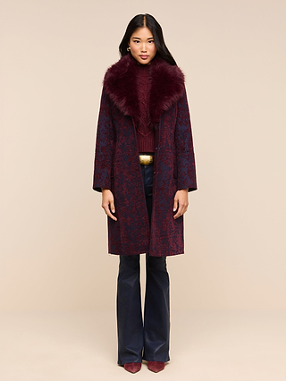 A woman stands facing forward wearing the Laney Jacquard Coat with a faux fur collar, paired with a matching turtleneck, dark pants, and burgundy shoes against a plain beige background.