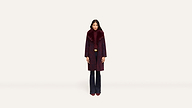 A woman stands facing forward, wearing a long, dark burgundy coat with a wide fur collar and matching burgundy shoes against a plain white background.