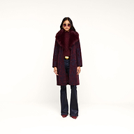 A woman stands against a plain white background wearing the Laney Jacquard Coat—a vintage-inspired burgundy coat with a large faux fur collar—paired with dark flared pants, a maroon top, pointed shoes, sunglasses, and a gold belt.