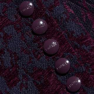 Five glossy, dark purple buttons are arranged vertically on a textured, deep burgundy and navy patterned fabric. The buttons have LAGMEY embossed on them, adding a distinctive touch to the Laney Jacquard Coat’s vintage-inspired design.