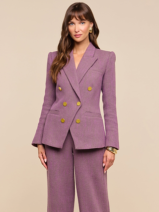 A woman with long brown hair wears the Kyomi Double-Breasted Blazer in mauve, featuring gold buttons, as she poses against a plain beige background. She accessorizes with golden hoop earrings and gold bangles on her left wrist.