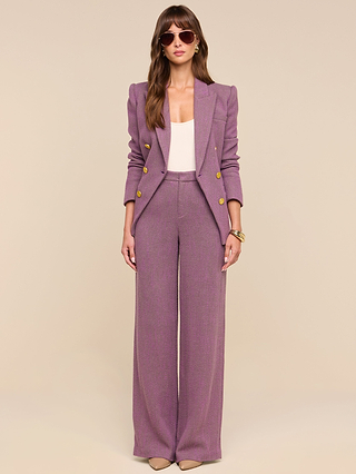 A woman stands against a beige background wearing the Kyomi Double-Breasted Blazer in mauve, paired with matching pants, a white top, nude heels, sunglasses, and a gold bracelet.