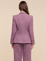 A woman with long brown hair stands facing away, wearing the Kyomi Double-Breasted Blazer in mauve, featuring gold buttons on the sleeves, against a plain light background.