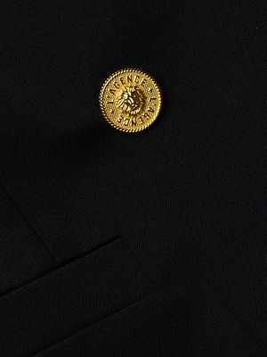 Close-up of a gold lion-embossed button on the Kyomi Double-Breasted Blazer by L'AGENCE, sewn near the breast pocket. The fine-textured black fabric and button detail showcase the sophisticated design of this women's blazer.