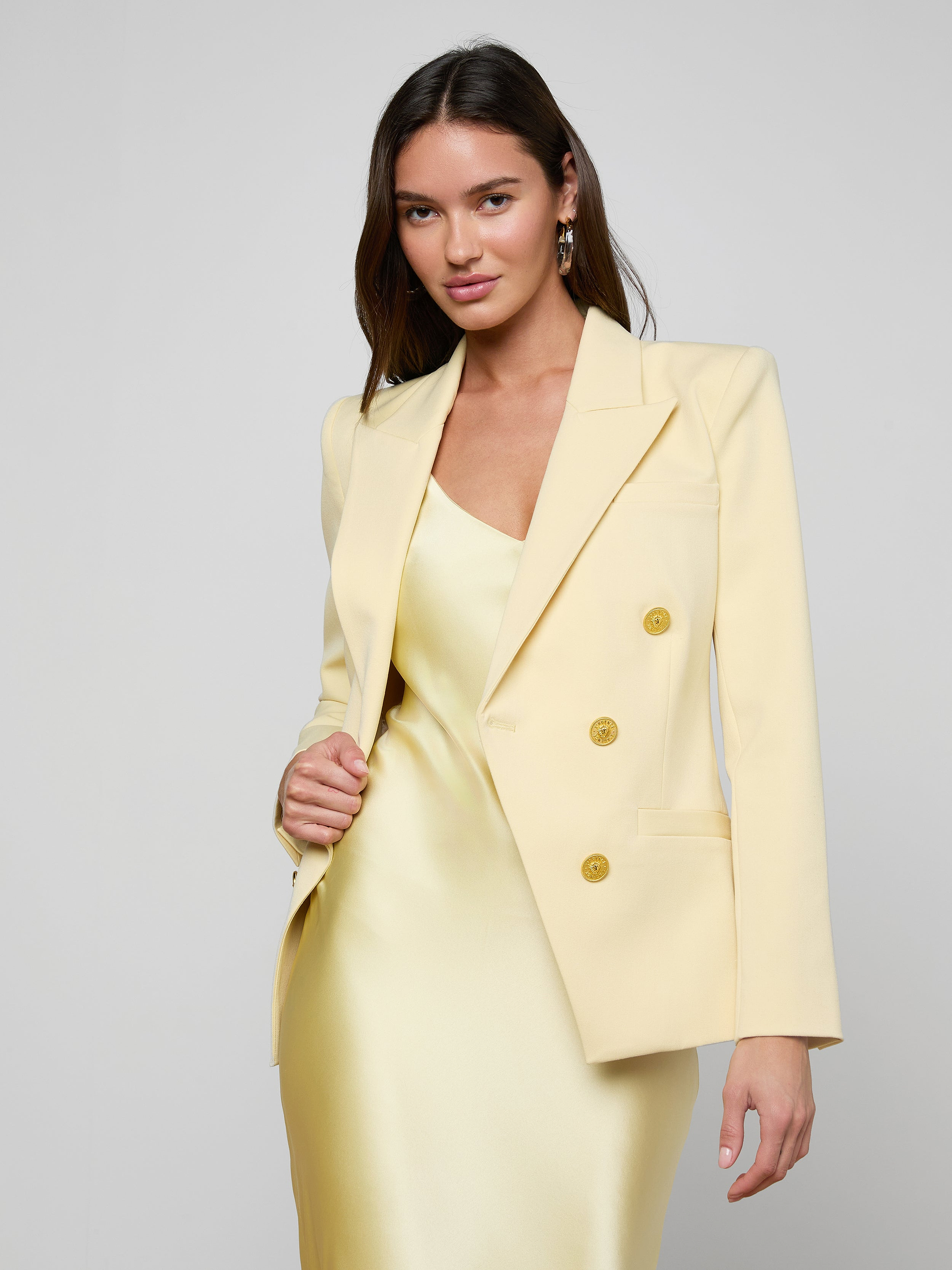 Wearing the Kyomi Double-Breasted Blazer over a matching satin dress, a woman stands confidently against a plain light background, looking directly at the camera.