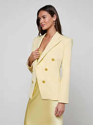 A woman in the Kyomi Double-Breasted Blazer and a matching dress stands against a plain white background, looking to the side with one hand touching her lapel.