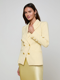 A woman wearing the Kyomi Double-Breasted Blazer in yellow with gold buttons and a matching skirt stands against a plain light background, looking confidently at the camera.
