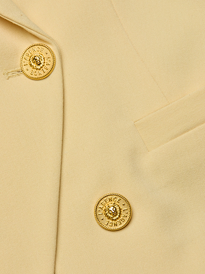 Close-up of the beige Kyomi Double-Breasted Blazer, showcasing two ornate gold buttons with raised lion head designs and text, positioned beside a welt pocket and highlighted stitching détails.