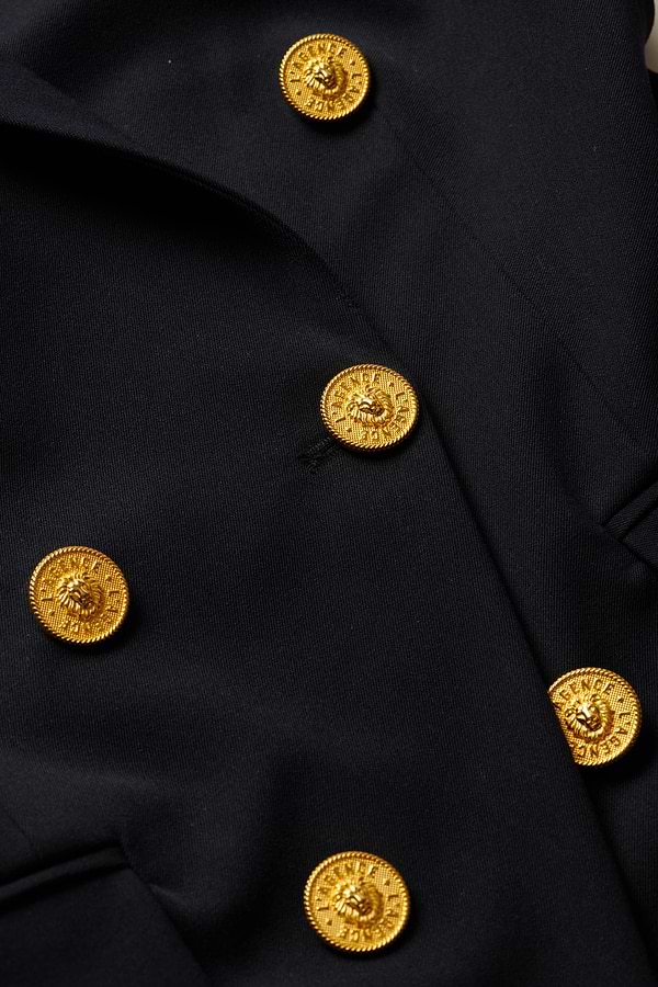 Close-up of the Kyomi Double-Breasted Blazer in black fabric, featuring four shiny gold buttons arranged diagonally. The buttons are embossed with a lion’s head design and have detailed edges.
