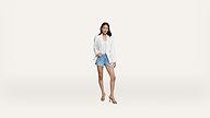 A woman stands confidently wearing a white blazer, white top, denim shorts, and beige heels against a plain white background.