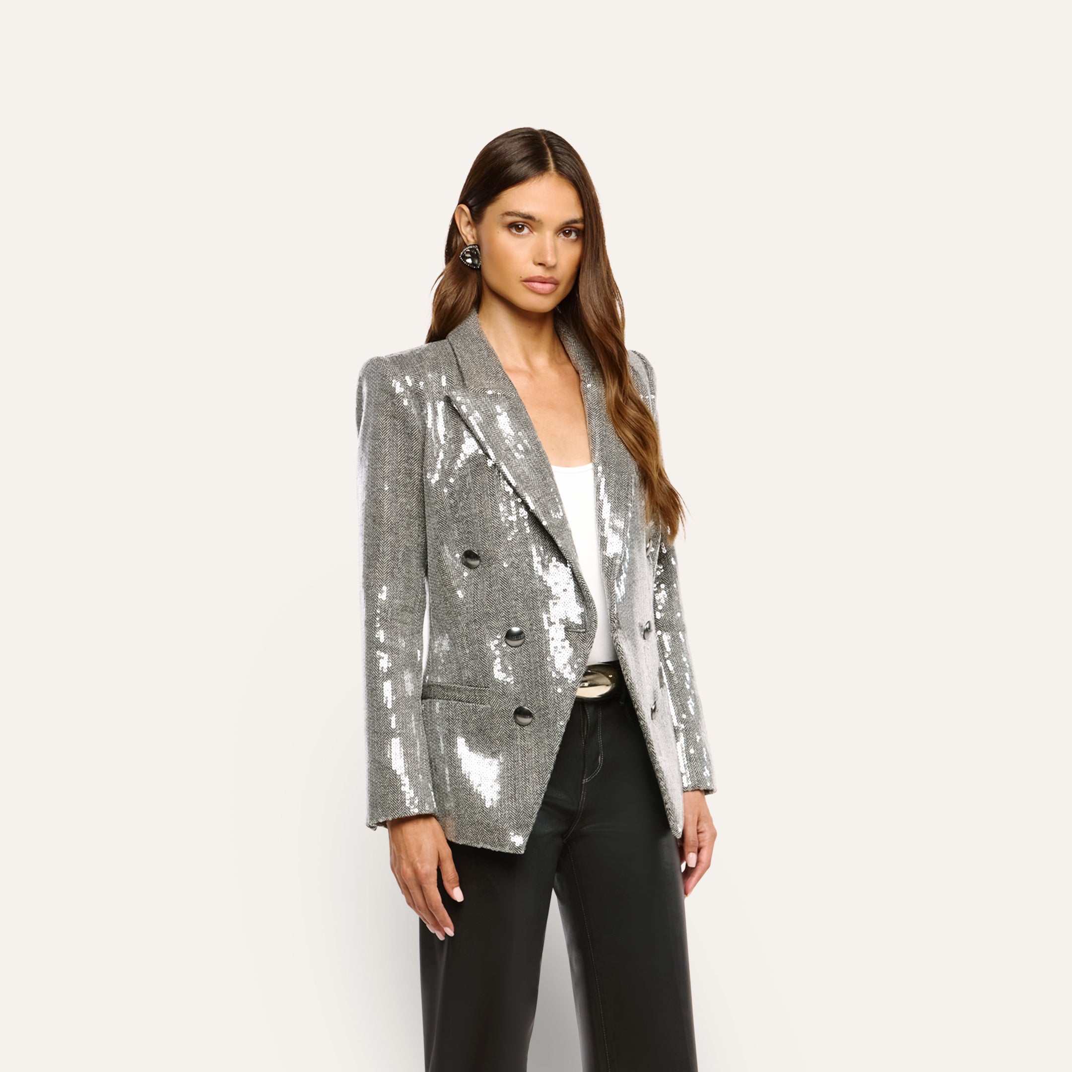 A woman wears a double-breasted, silver sequin Kyomi Sequined Blazer over a white top and black trousers.