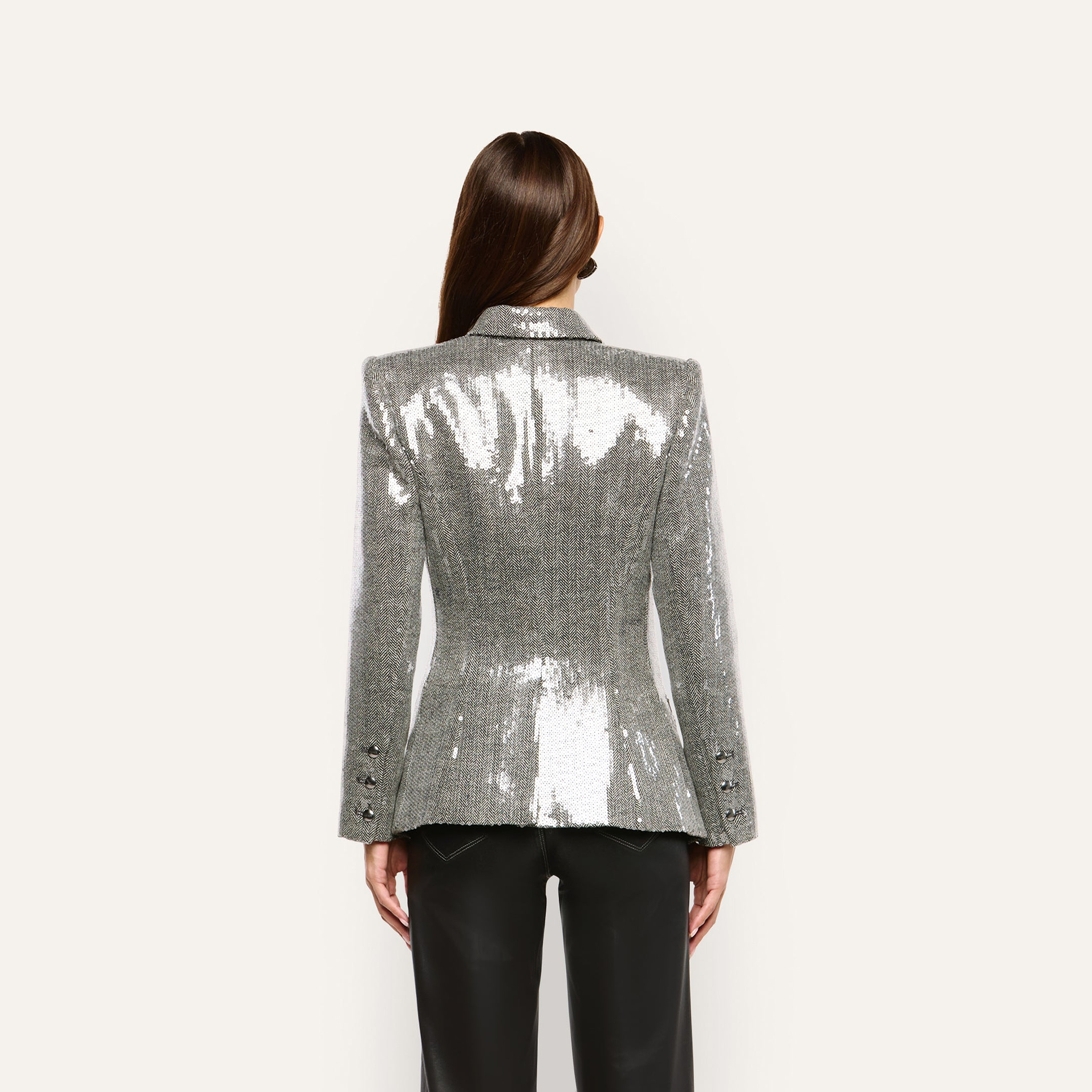 Back view of a person wearing a silver, double-breasted Kyomi Sequined Blazer with structured shoulders and black trousers.