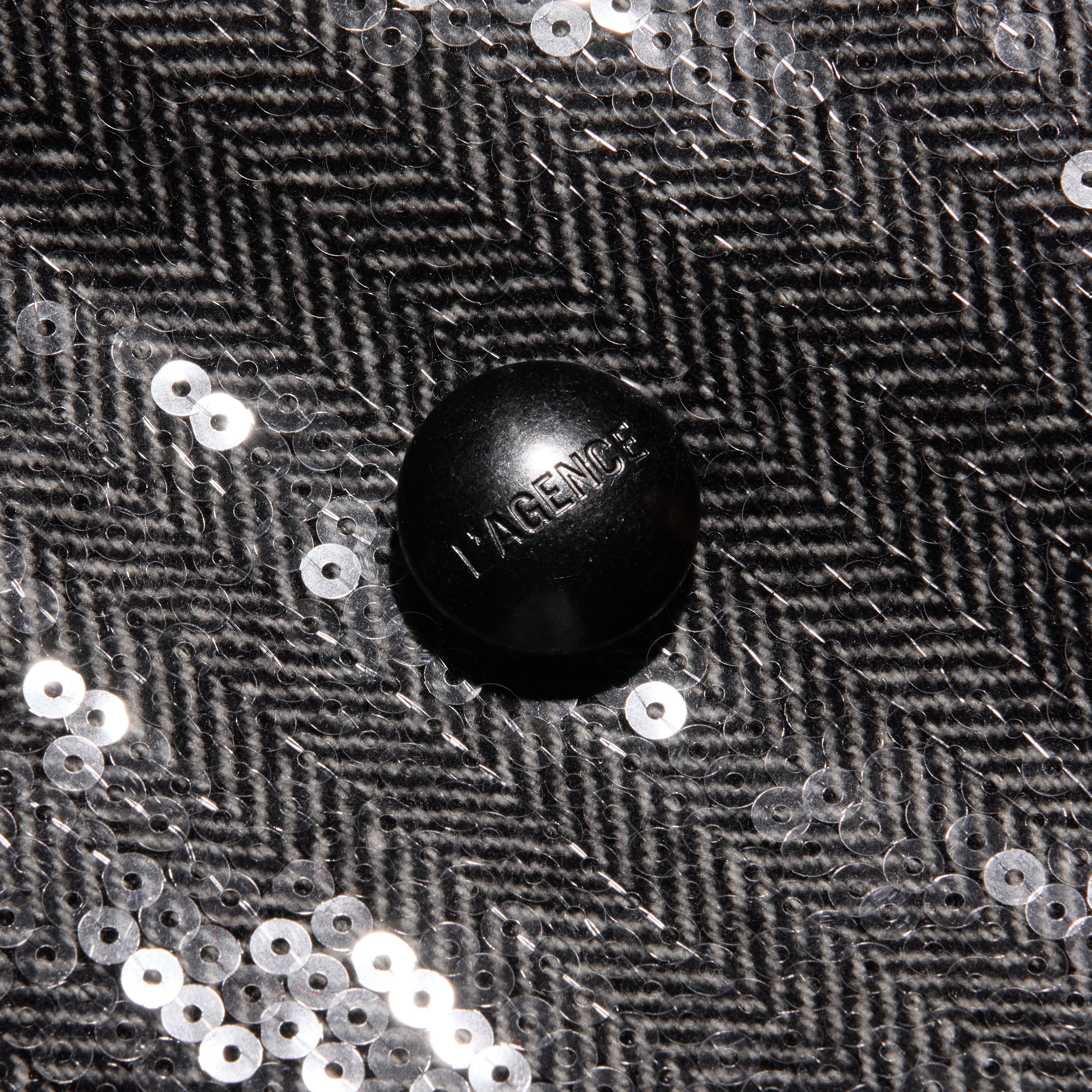 A black button featuring the word LAGENCE centered on a grey herringbone Kyomi Sequined Blazer with scattered silver sequins.
