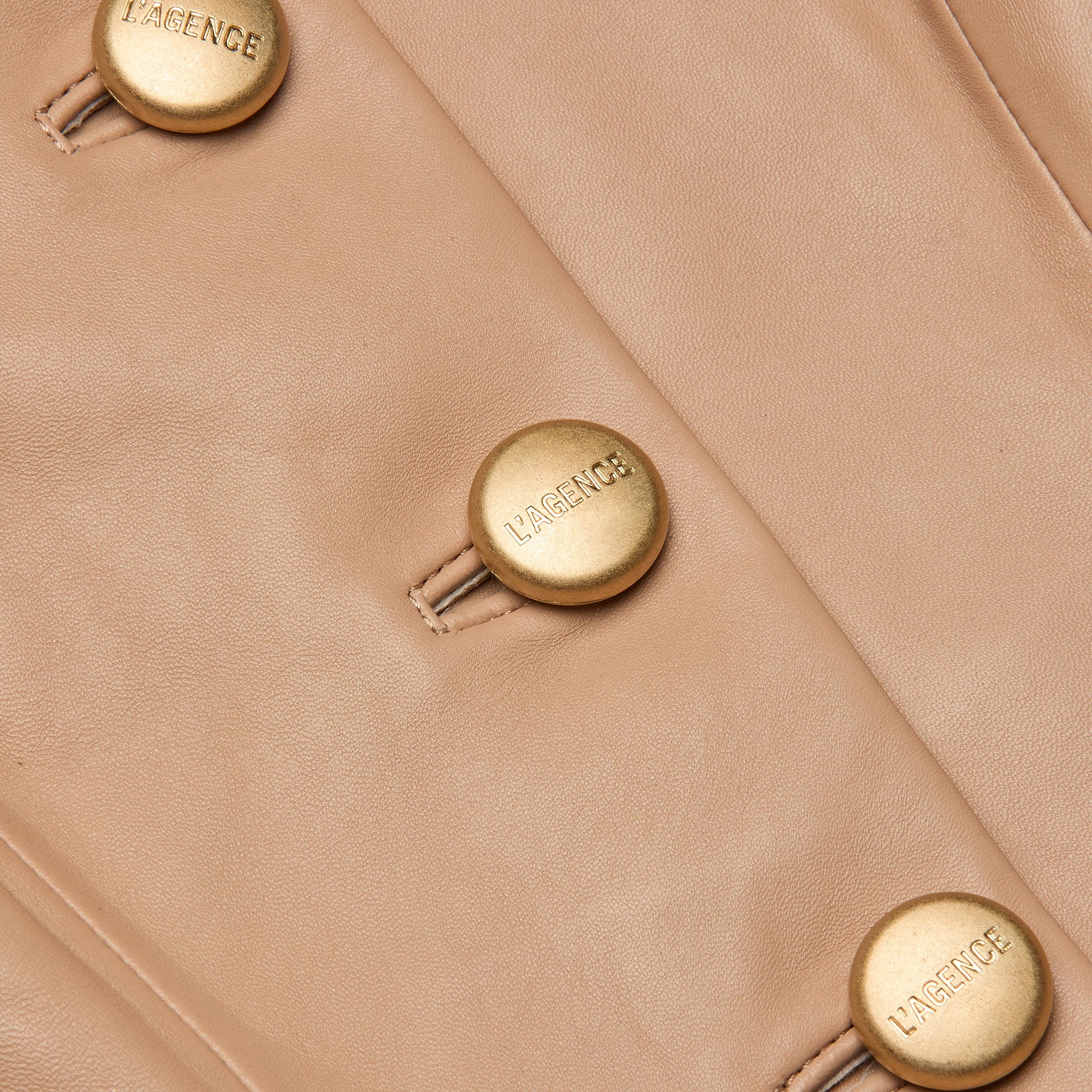 Close-up of the Mariella Leather Jacket in cappuccino leather, featuring gold buttons engraved with L’AGENCE. The buttons are sewn in a vertical line, accentuating the chic jacket’s elegant appeal.
