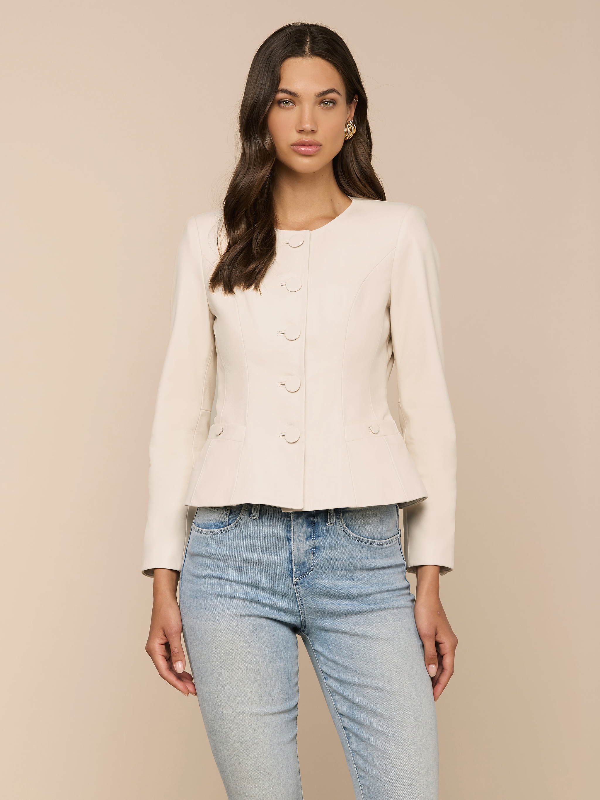 A woman wearing the Mariella Leather Jacket—a fitted, cream-colored, collarless design—paired with light blue jeans stands facing forward against a plain light background.
