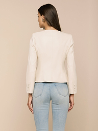 A woman facing away from the camera models the Mariella Leather Jacket—a chic, cream-colored, collarless design—paired with light blue jeans against a plain white background.