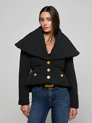 A woman wearing the Pippa High Collar Jacket, a black puffer style with a sculptural high collar and gold buttons, paired with blue jeans, stands against a plain light gray background.