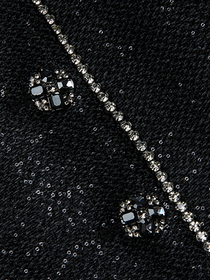 Close-up of the Zell Sequined Tweed Jacket by L'AGENCE: textured black fabric with two decorative round black and clear jewel buttons and a diagonal line of sparkling rhinestones.