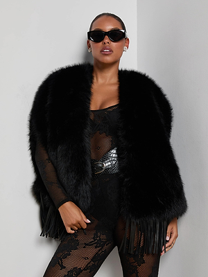 A person wearing black cat-eye sunglasses, the L'AGENCE Nathalia Faux Fur Cape, and a black lace bodysuit with a textured belt stands confidently against a white wall.