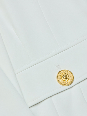 Close-up of the Nixie Cardigan Jacket in white fabric, featuring wide bell sleeves and a decorative gold button with an embossed design sewn onto the seam, lending elegance to this minimalist piece.