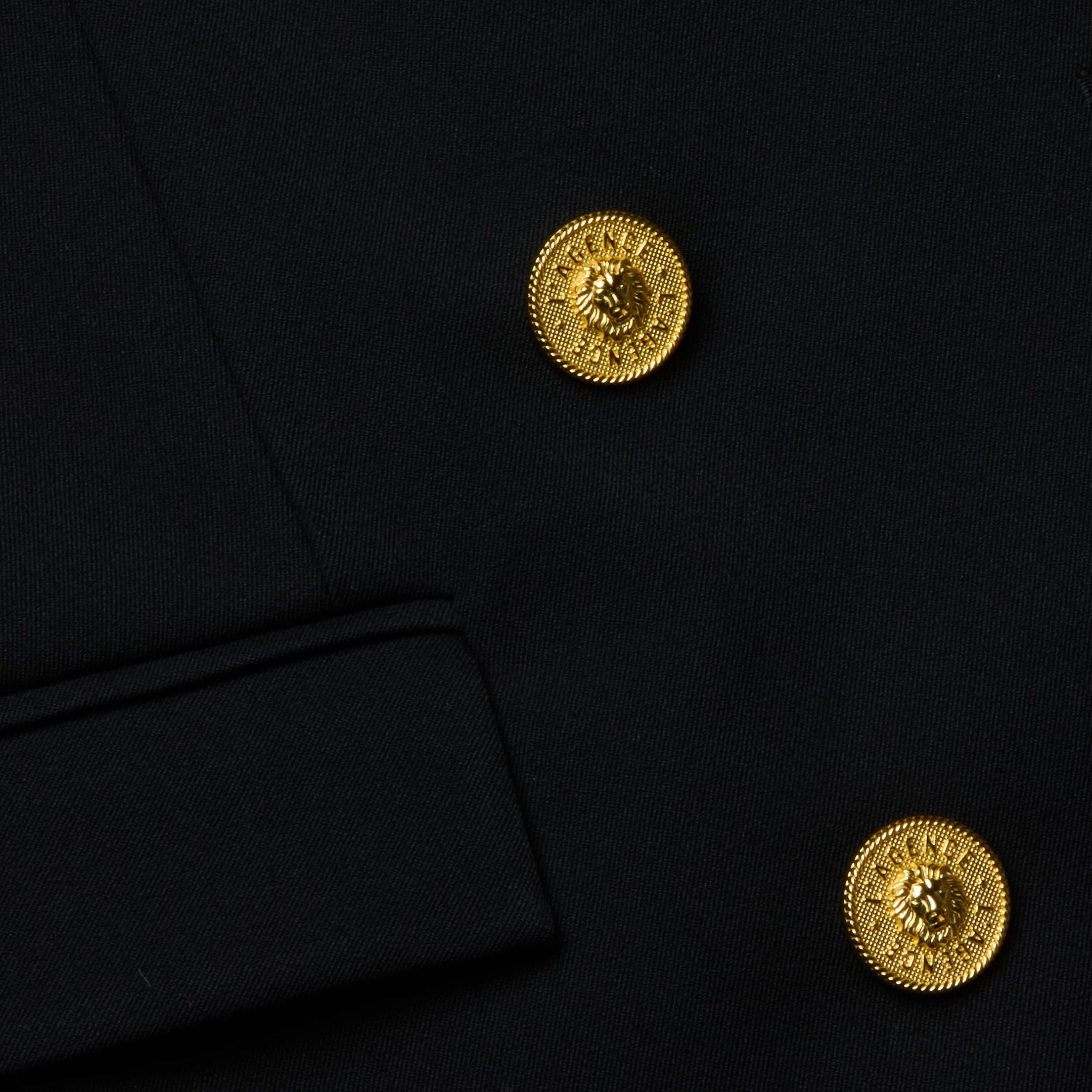 Close-up of the Cambrie Oversized Blazer in black, showcasing two shiny gold crest-engraved buttons and a visible sleeve cuff edge.