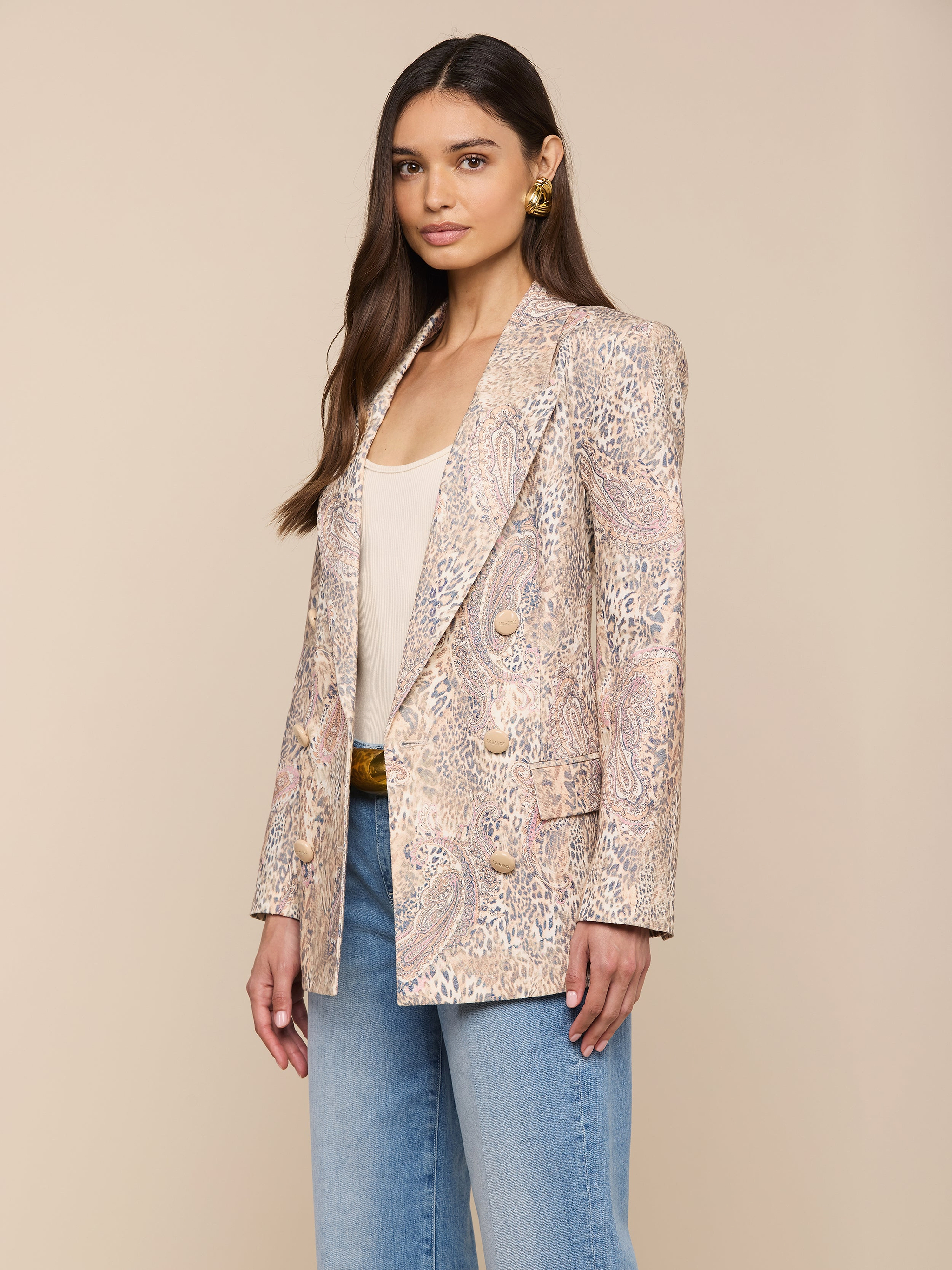 Une femme aux longs cheveux bruns porte le blazer Cambrie Oversized Linen-Blend sur un haut beige et un jean bleu, sur un fond neutre.