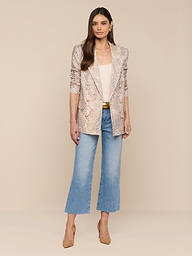 Une femme est debout, de face, portant le blazer Cambrie Oversized Linen-Blend, un top beige clair, un jean bleu, une ceinture dorée et des talons beiges sur un fond beige uni.
