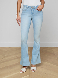 A person wearing Taney Low-Rise Flare Jeans in light blue stretch denim and white heeled sandals stands against a plain background, with only the lower half of the body visible.